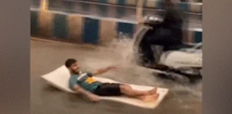 Man floats on mattress, waterlogged road, heavy rain
